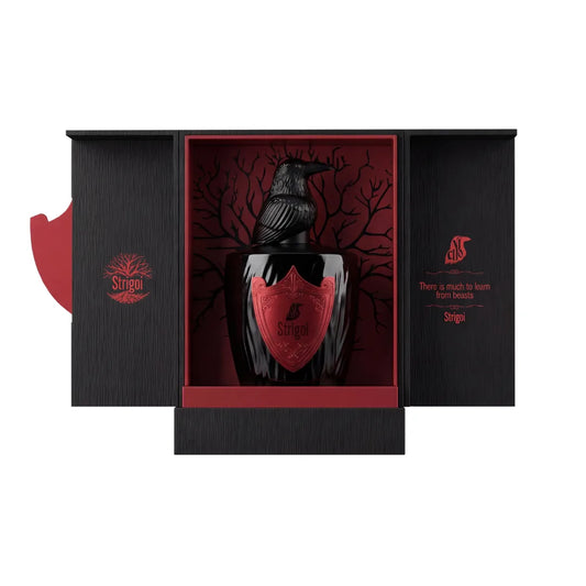 Estuche abierto de Strigoi, El Nicho, con el frasco de tapón de cuervo sobre fondo rojo con árbol y la frase There is much to learn from beasts