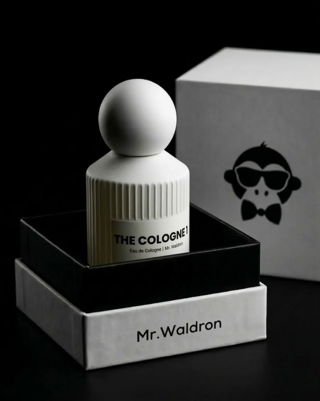 Perfume The Cologne 1 de Mr. Waldron en frasco blanco minimalista con tapón esférico sobre caja de lujo negra y packaging elegante